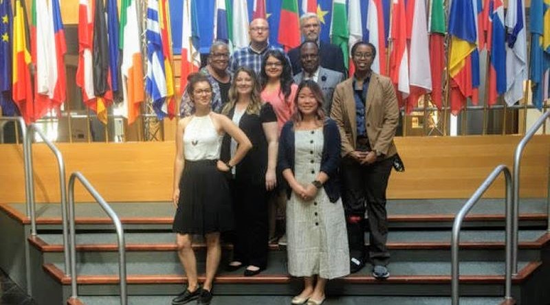 Group of people posing on stairs in front of international flags.
