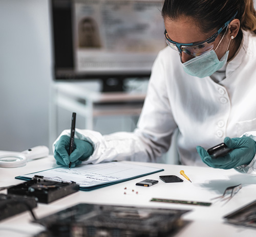 A woman in a lab coat and gloves analyzes data on a computer in a criminology research setting.