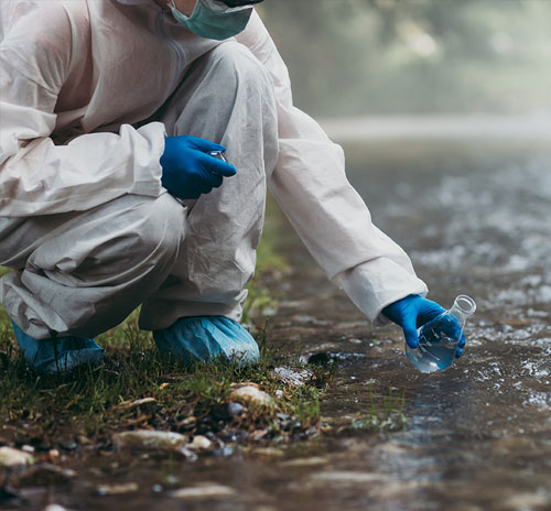 Environmental Studies researcher in protective gear collecting a water sample from a stream for ecological testing and analysis.