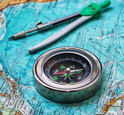 Compass and drawing compass resting on a colorful world map, symbolizing tools used in the study of geography and navigation.