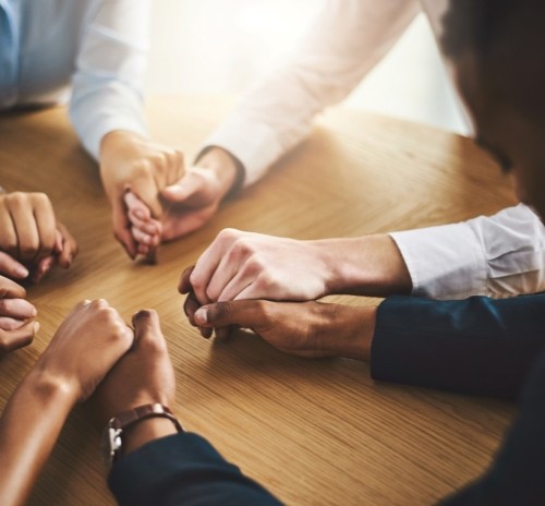 Group of people holding hands around a table, symbolizing unity, community, or shared spiritual practice.