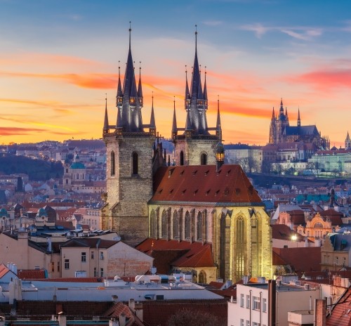 Scenic view of Prague’s Gothic architecture at sunset, with church spires and rooftops bathed in warm light, emphasizing cultural and historical richness.