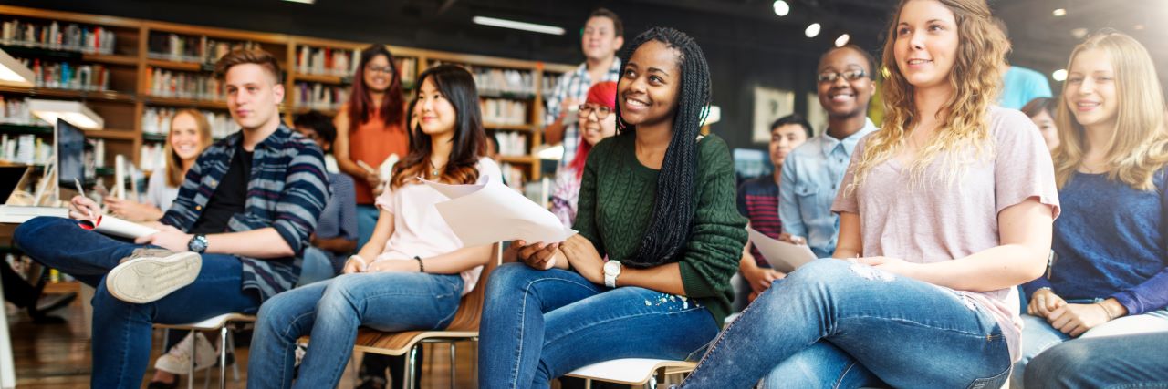 Students smiling and sitting in chairs in a library setting.