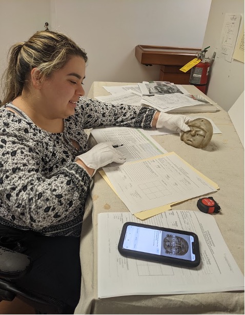 A woman in a lab with a folder and cellphone, examining an artifact.
