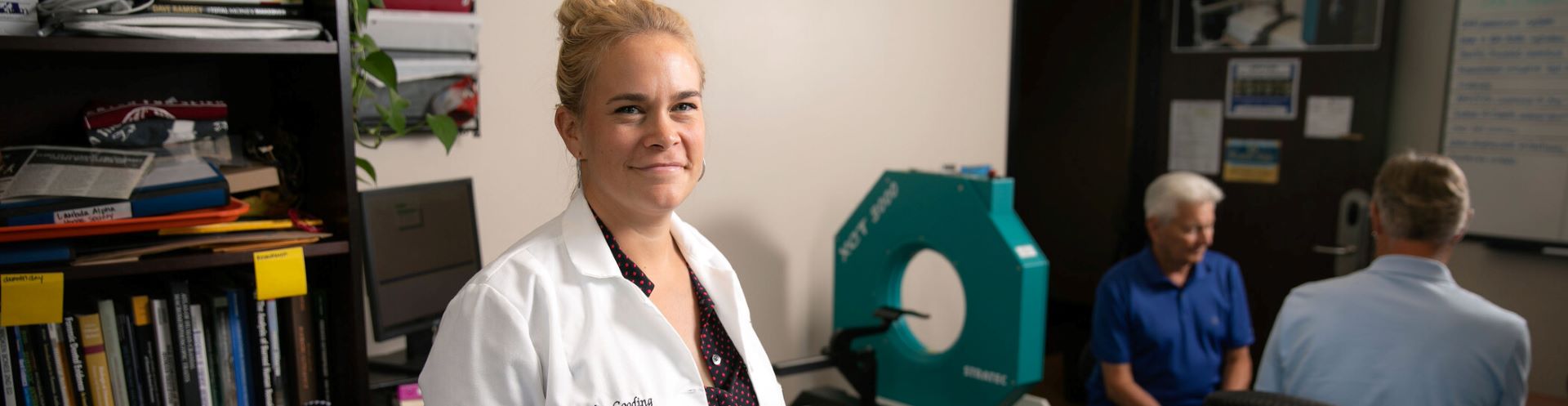 A woman wearing a lab coat and standing next to a medical scanner