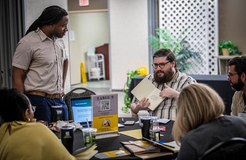 Photo of student explaining his project to a group of students at a table.