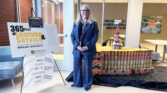 A woman standing in a blue suit in front of a display of canned goods.