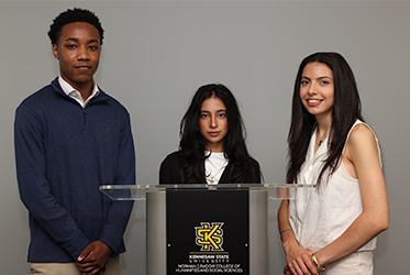 KSU students Jaylan Conwell, Zainab Wajid, and Silvia Prisco stand around a podium with Kennesaw State logo