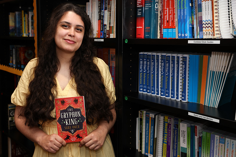 Sara Omer holding her book in the library