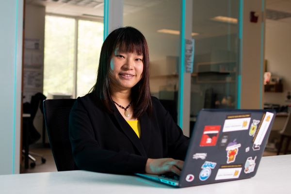 A woman smiling while using a laptop, in a classroom setting.