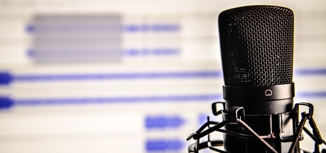 Close-up of a professional microphone with a blurred audio editing screen in the background