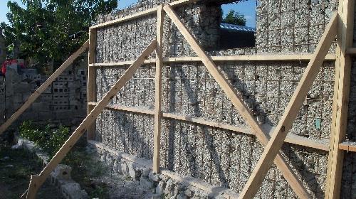  / A partially constructed wall made of wire mesh filled with rocks, supported by wooden braces.