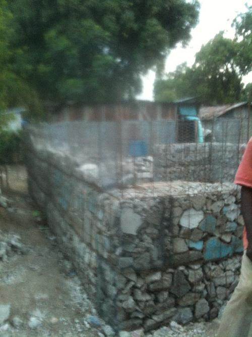  / A stone foundation wall under construction, surrounded by wire mesh