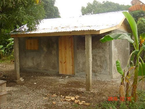  / Simple, small concrete house with a corrugated metal roof, wooden door, and window