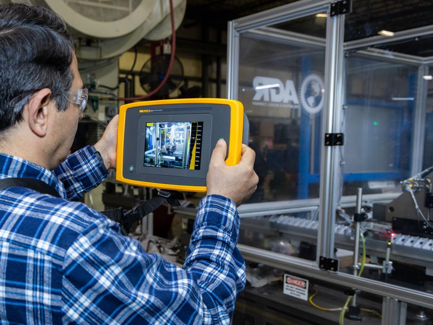 / Person holding a yellow and black diagnostic device showing machinery on its screen. 

