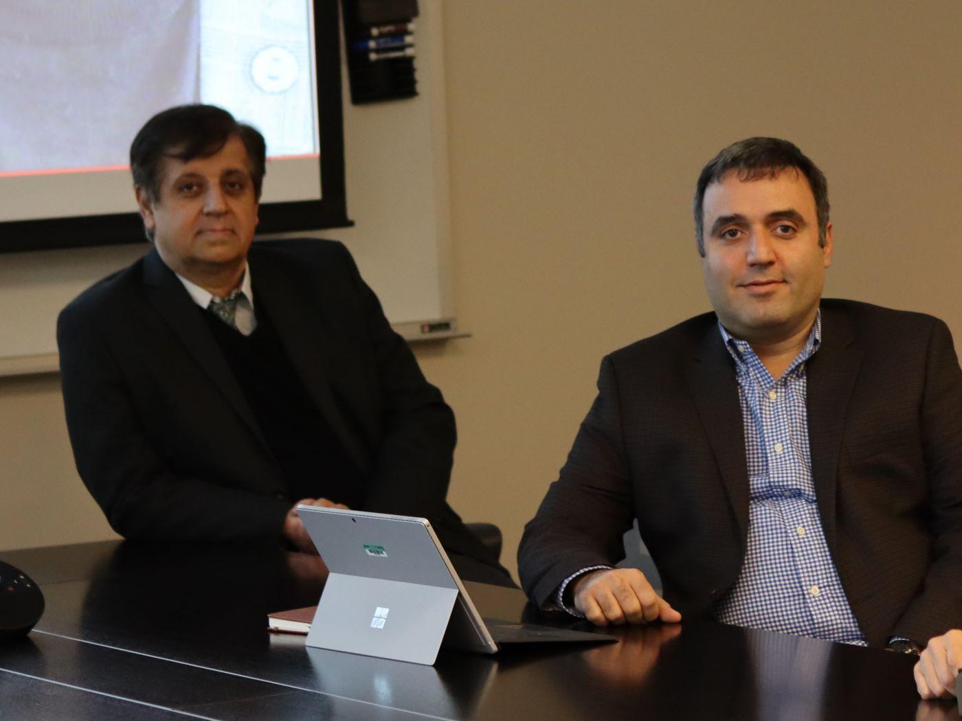  / Two men sitting at a table with a laptop in an office setting 
