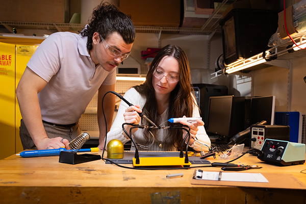 man watching woman using saudering iron