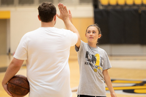 A young girl giving a high-five to a coach on a basketball court.