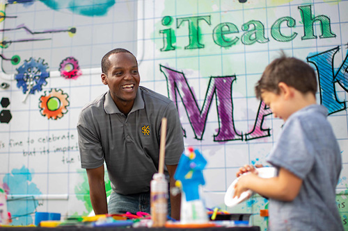 A smiling educator engaging with a young boy during a hands-on activity.