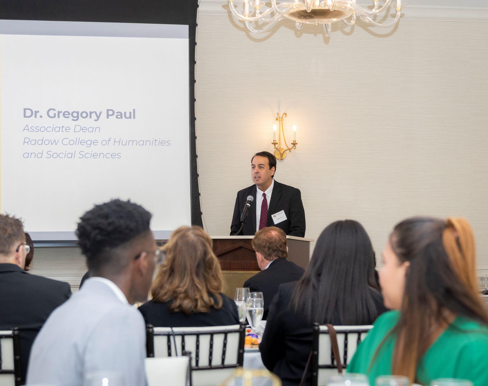 International Achievement Awards and Scholarship Ceremony 2026 / Gregory Paul speaking behind a podium. 