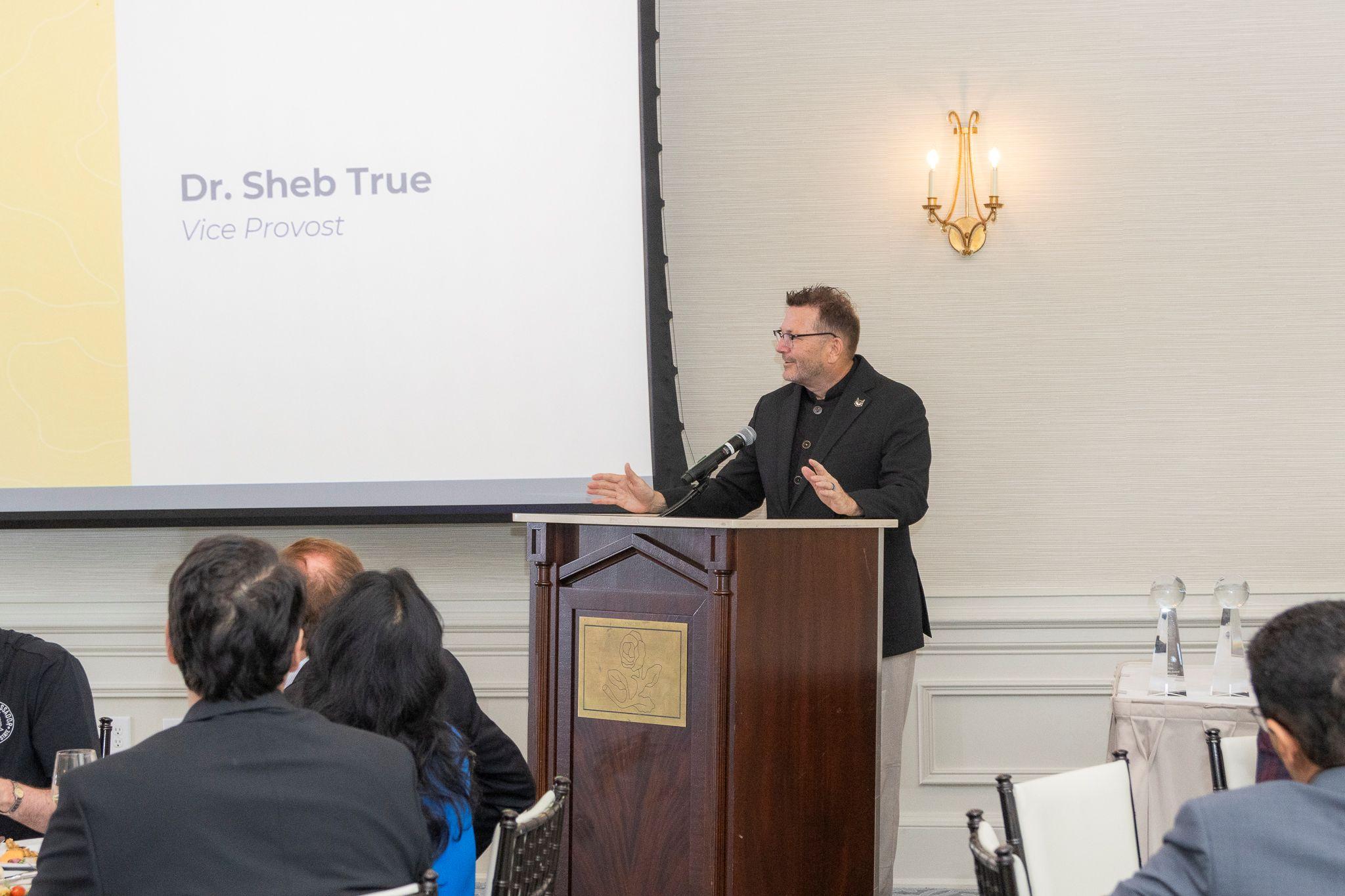 International Achievement Awards and Scholarship Ceremony 2026 / Sheb True speaks behind a podium. 