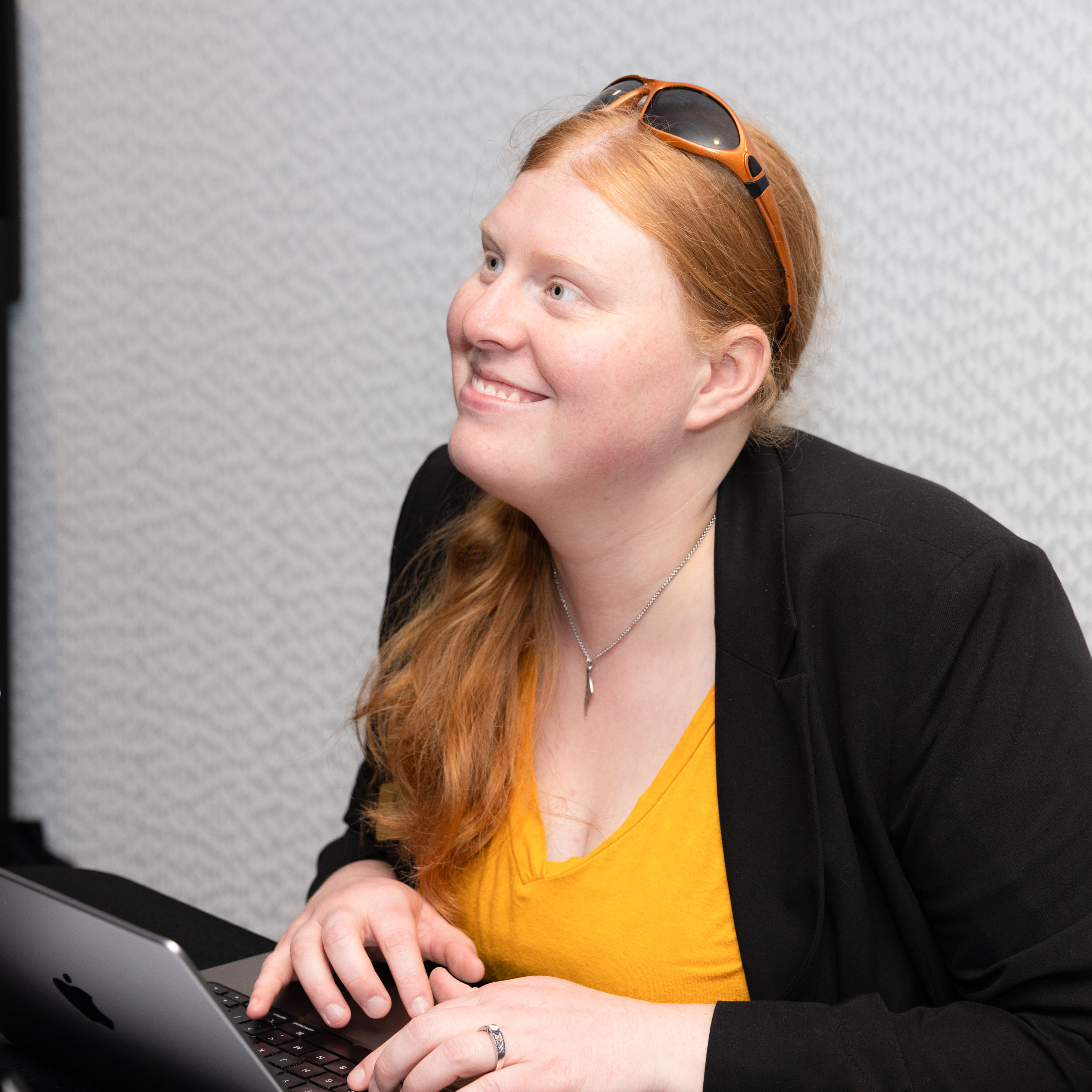 female staff member in yellow shirt smiling looking up away from computer