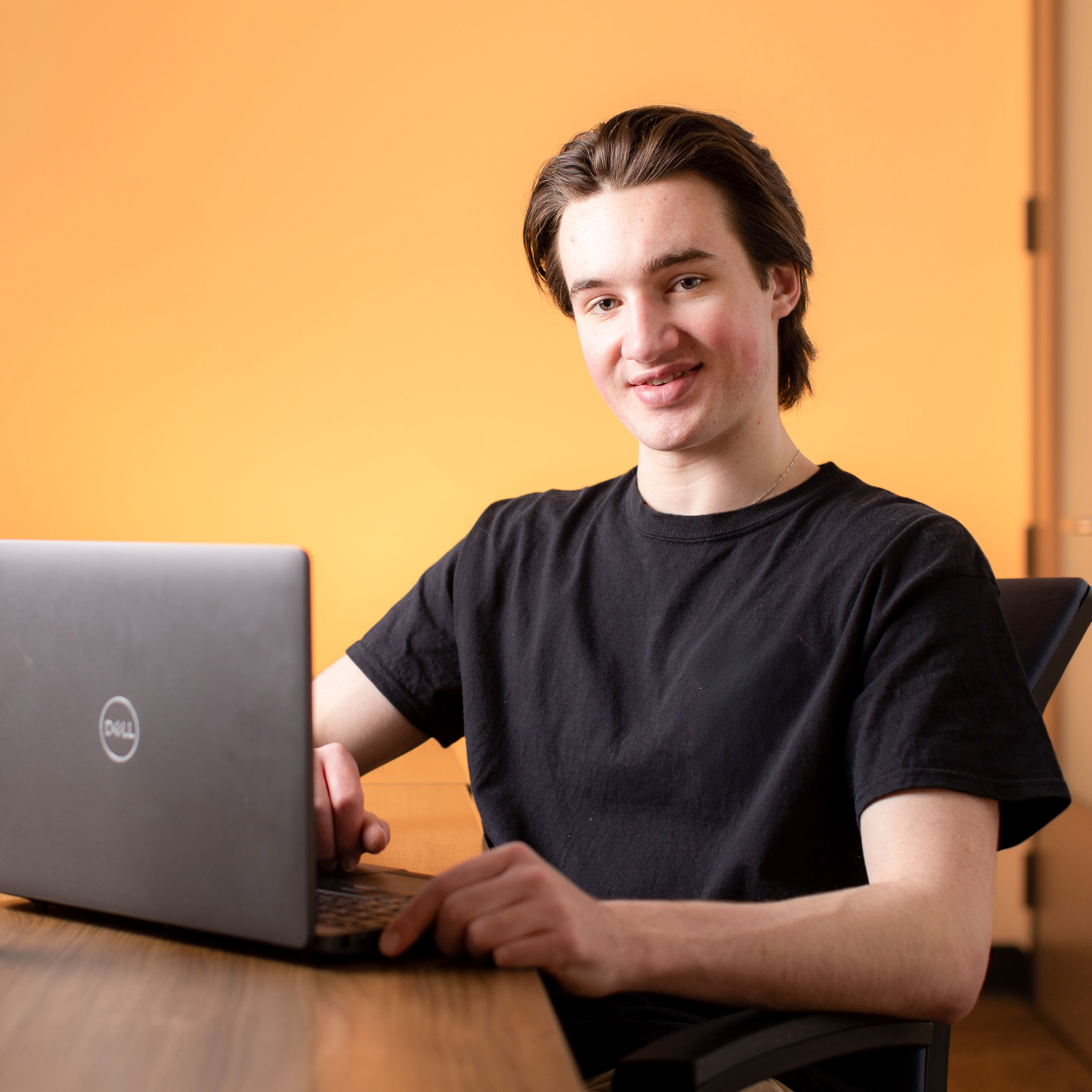 male student in black shirt smiling at computer