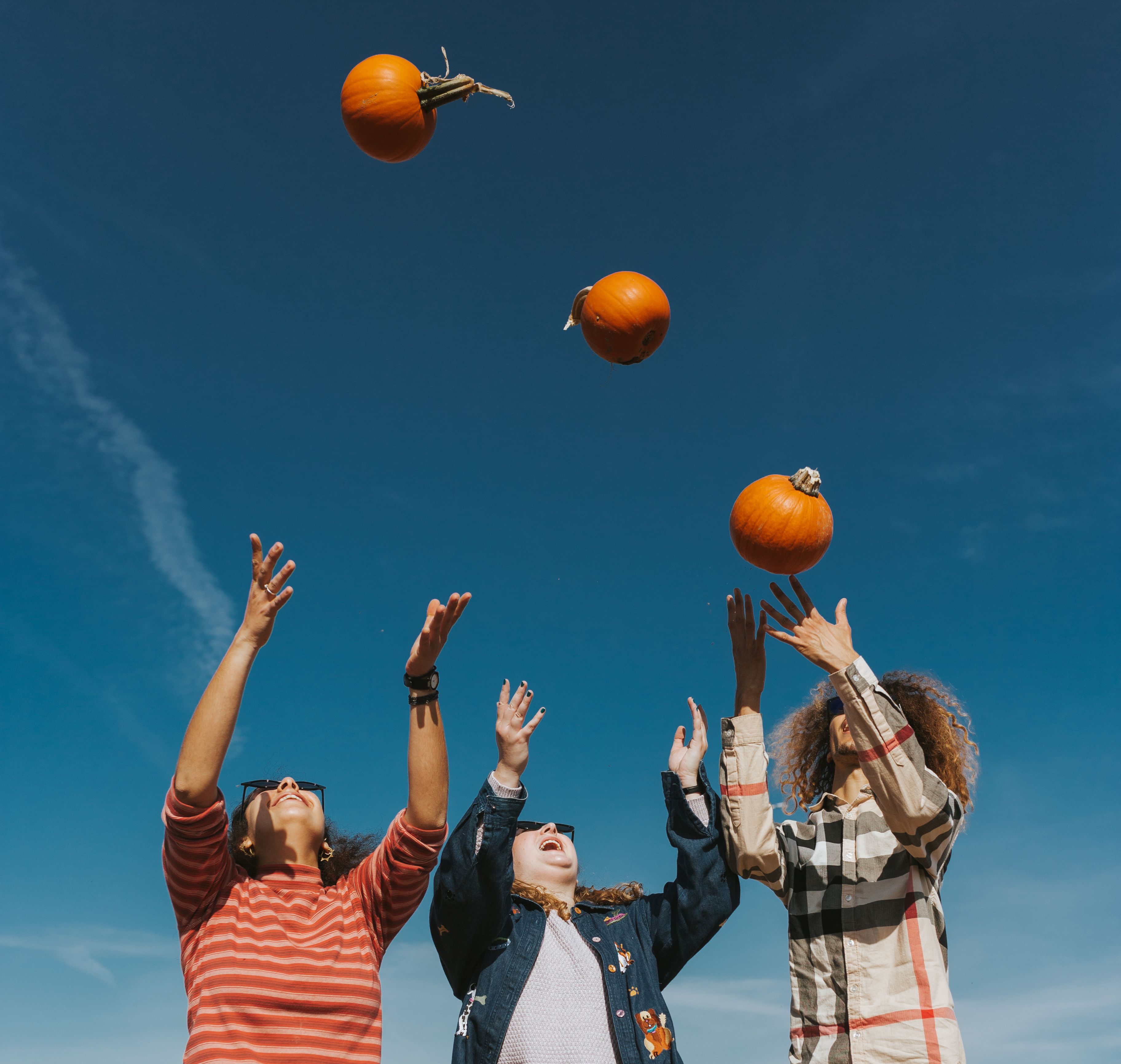 three people throwing pumpkins in the air