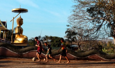 three boys run down the street kicking a soccer ball