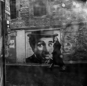Image of a woman walking on the sidewalk past a graffiti painting of Charlie Chaplin