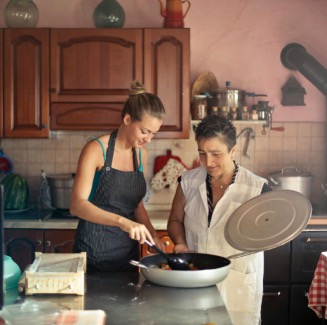 two women in a kitchen, one of them stirring ingredients in a skillet