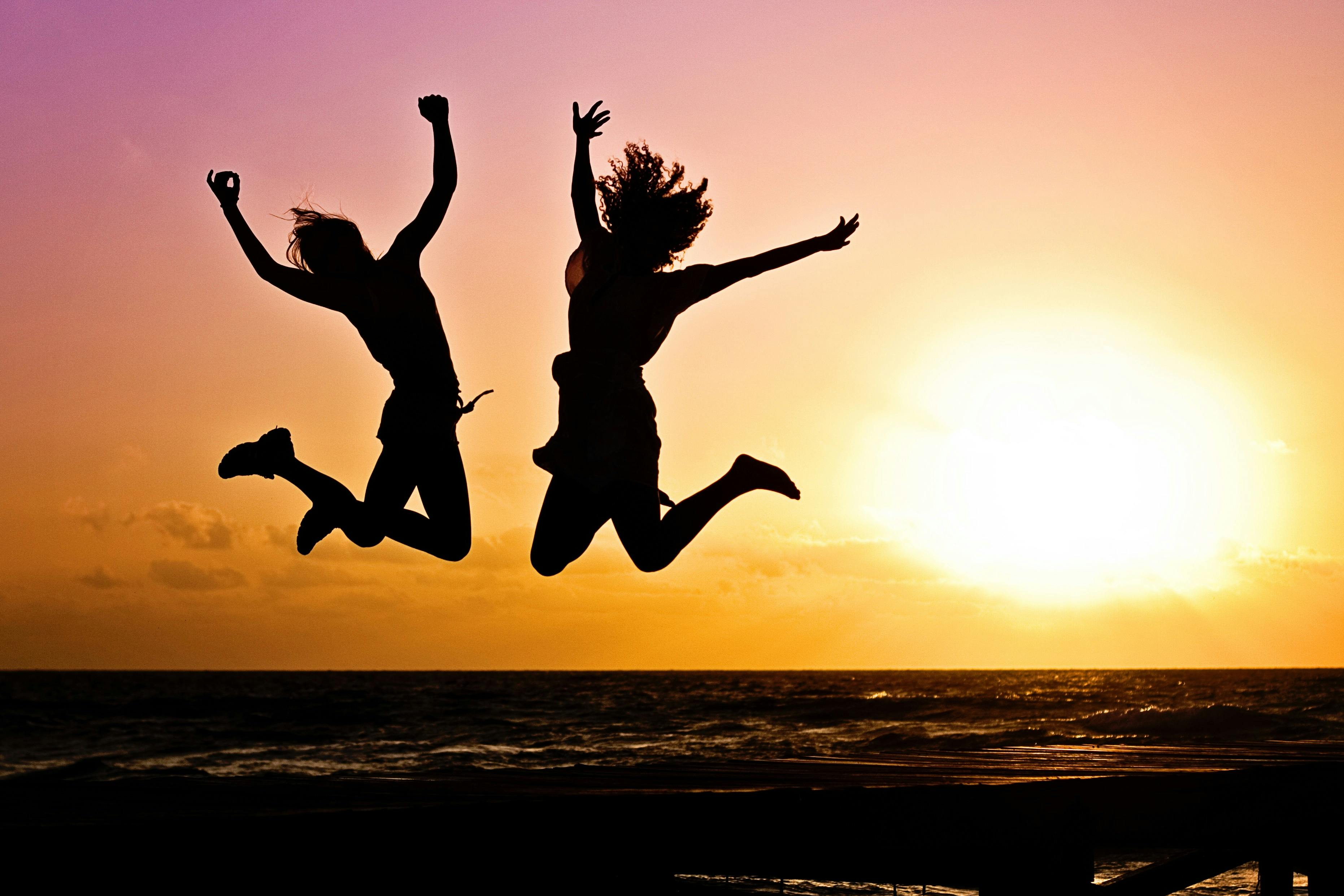 silhouette of two people jumping in the air in excitement during a sunset