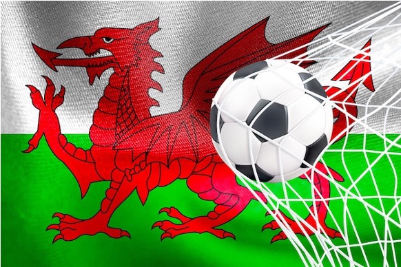The Welsh Flag with red, white, and green horizontal stripes and a soccer net in front catching a soccer ball