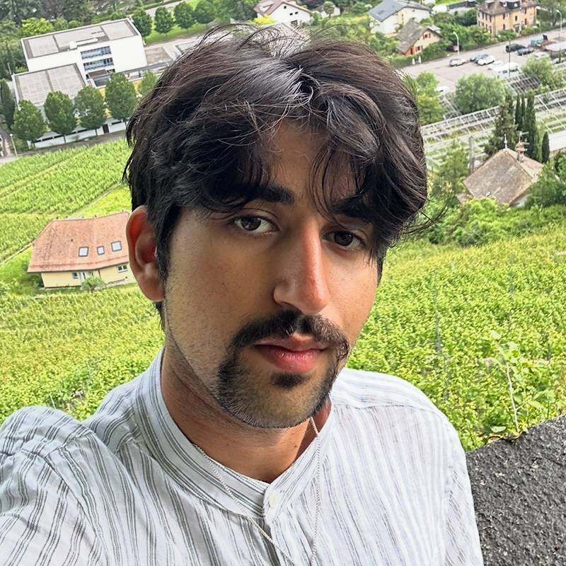 Daniel poses for a selfie with vineyards and a village visible in the background.