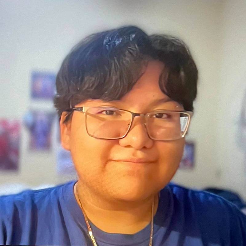 Close-up portrait of Sam wearing glasses and a blue shirt indoors with a softly blurred background.