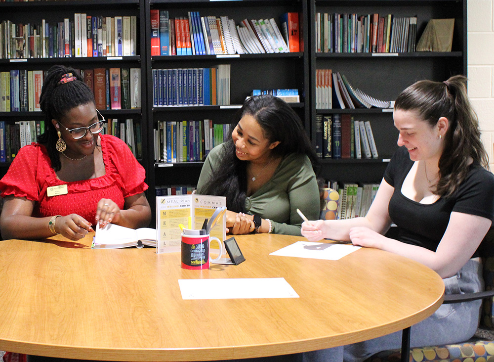 three students sitting at a table working on their paper