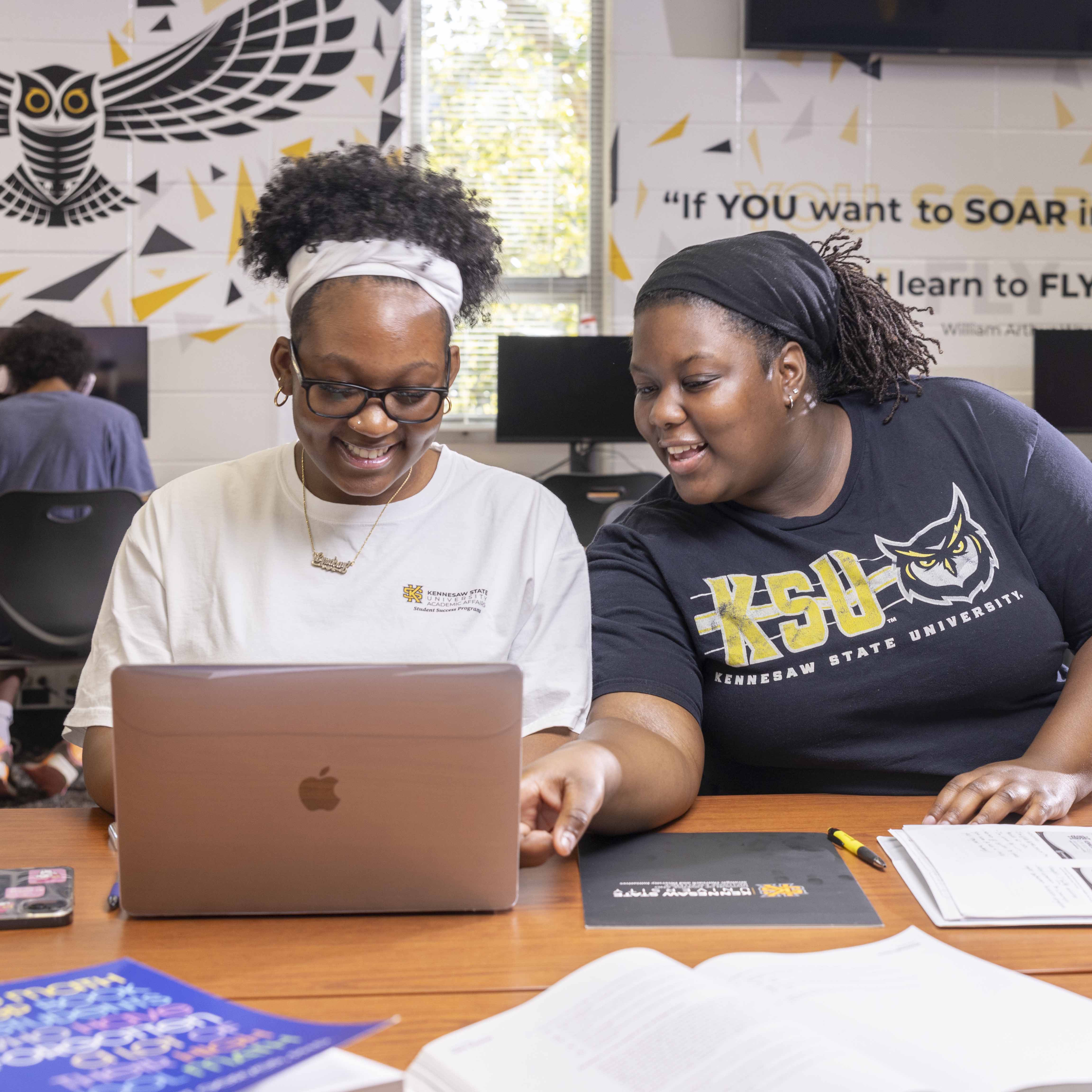 two females in ksu swag smiling looking at computer