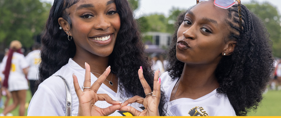 Two smiling students in white shirts with a "FLY" logo pose outdoors at Kennesaw State University.
