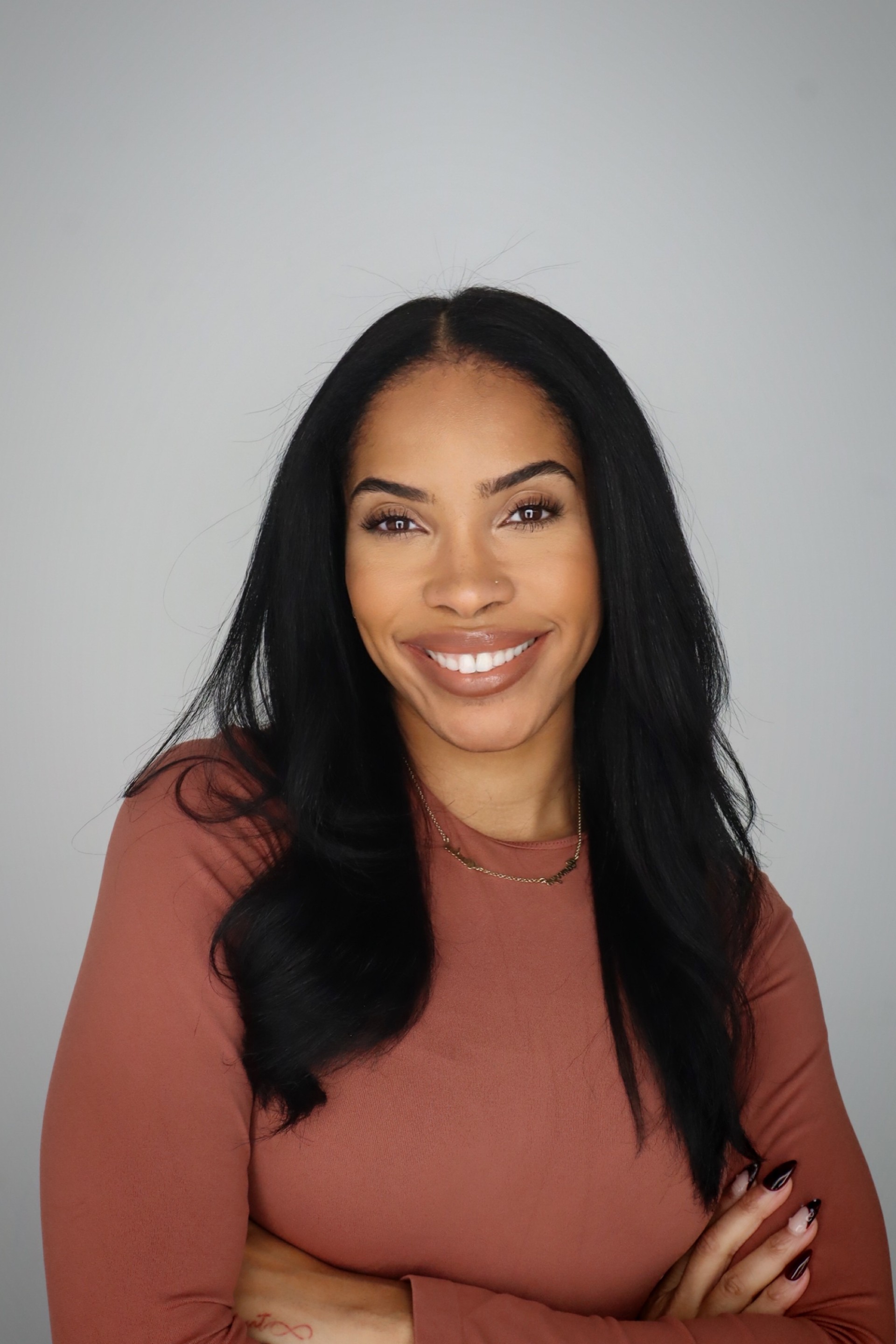 Headshot image of Alondra Givers. Person with long black hair wearing a rose-colored
                                    top, arms crossed, against a light gray background.