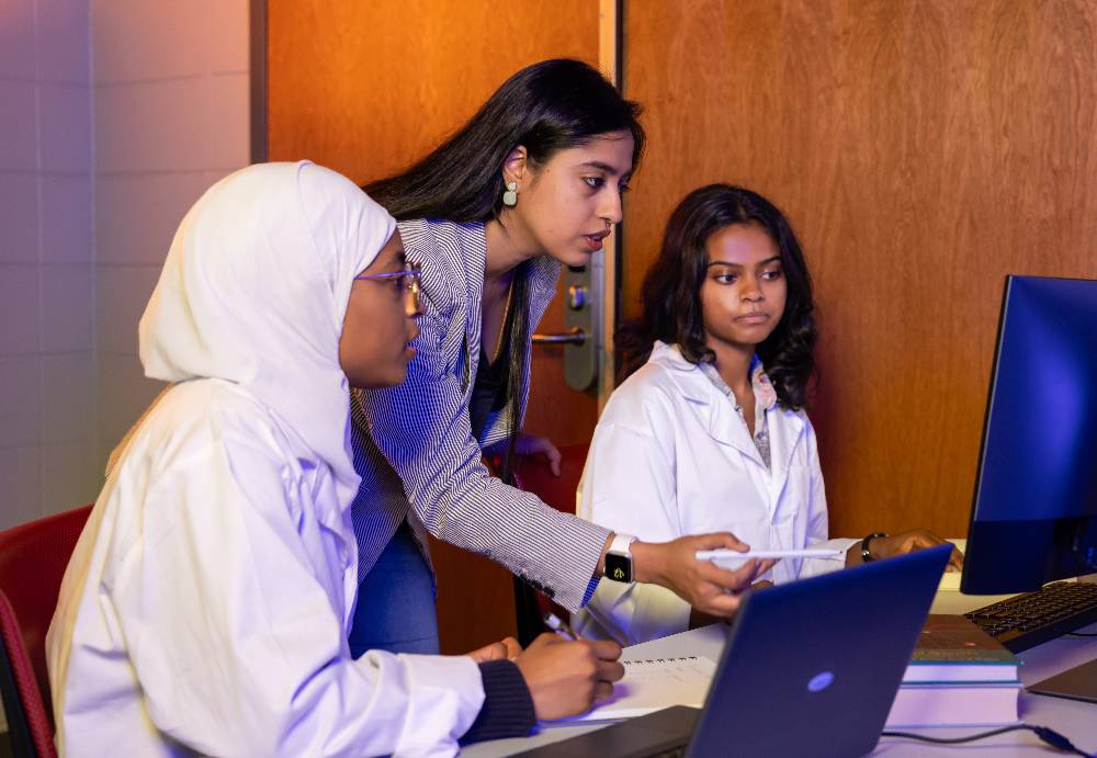 two students and their professor looking at ai software on a desktop monitor