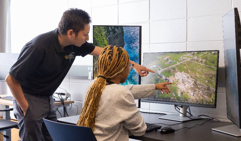 a student and professor pointing at AI software on a desktop computer screen