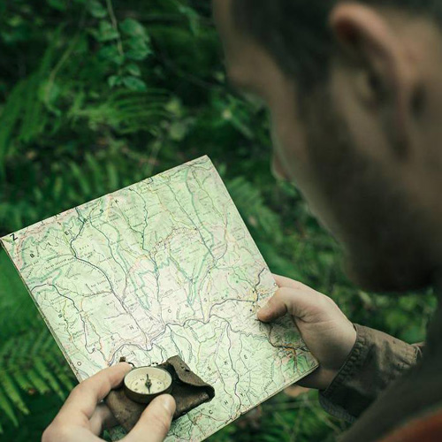 A person in the woods examines a map and compass, symbolizing metacognition in self-directed learning.