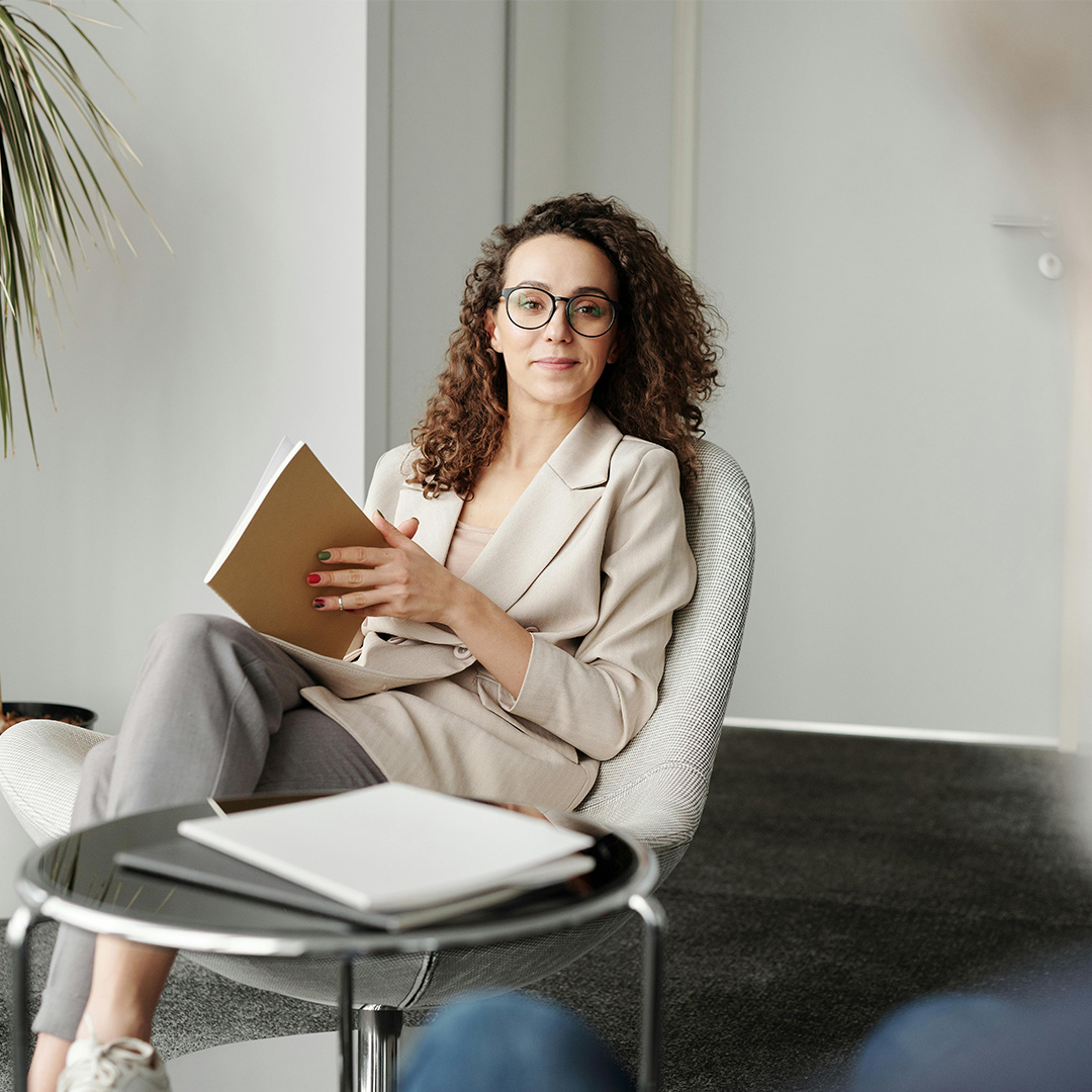 female sitting in chair with glasses and book in her hand