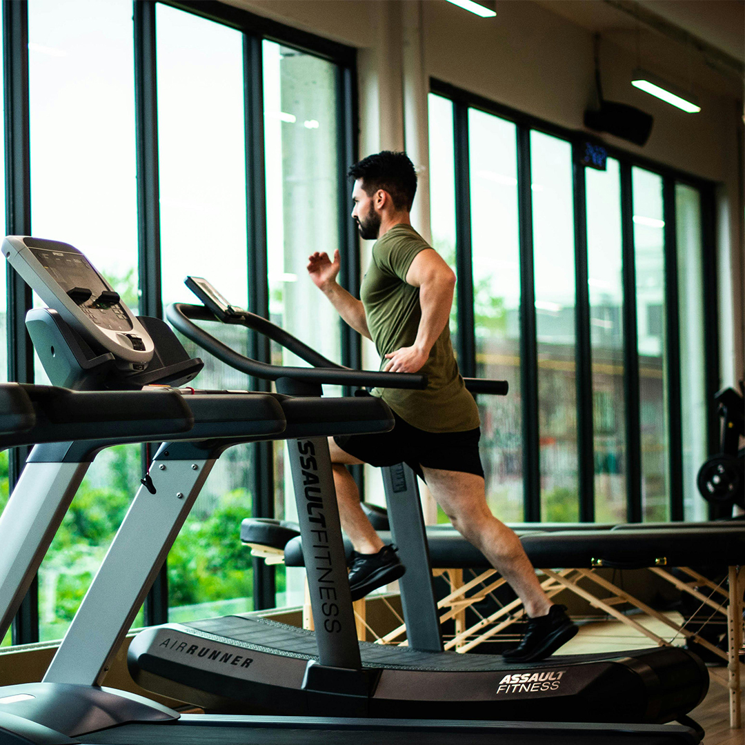 male working out on treadmill in gym with large windows