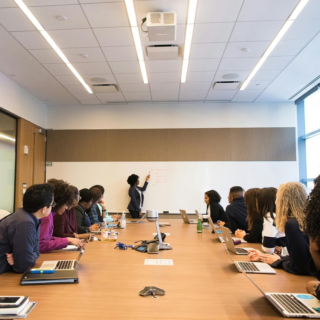 group of people sitting in board meeting with female speaker