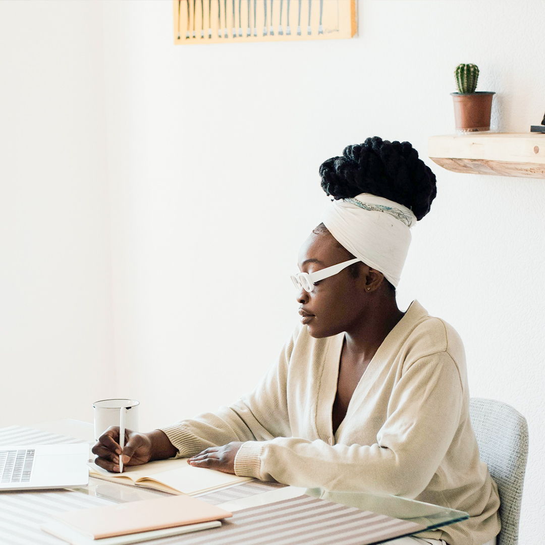 female at home office desk journaling and typing on computer