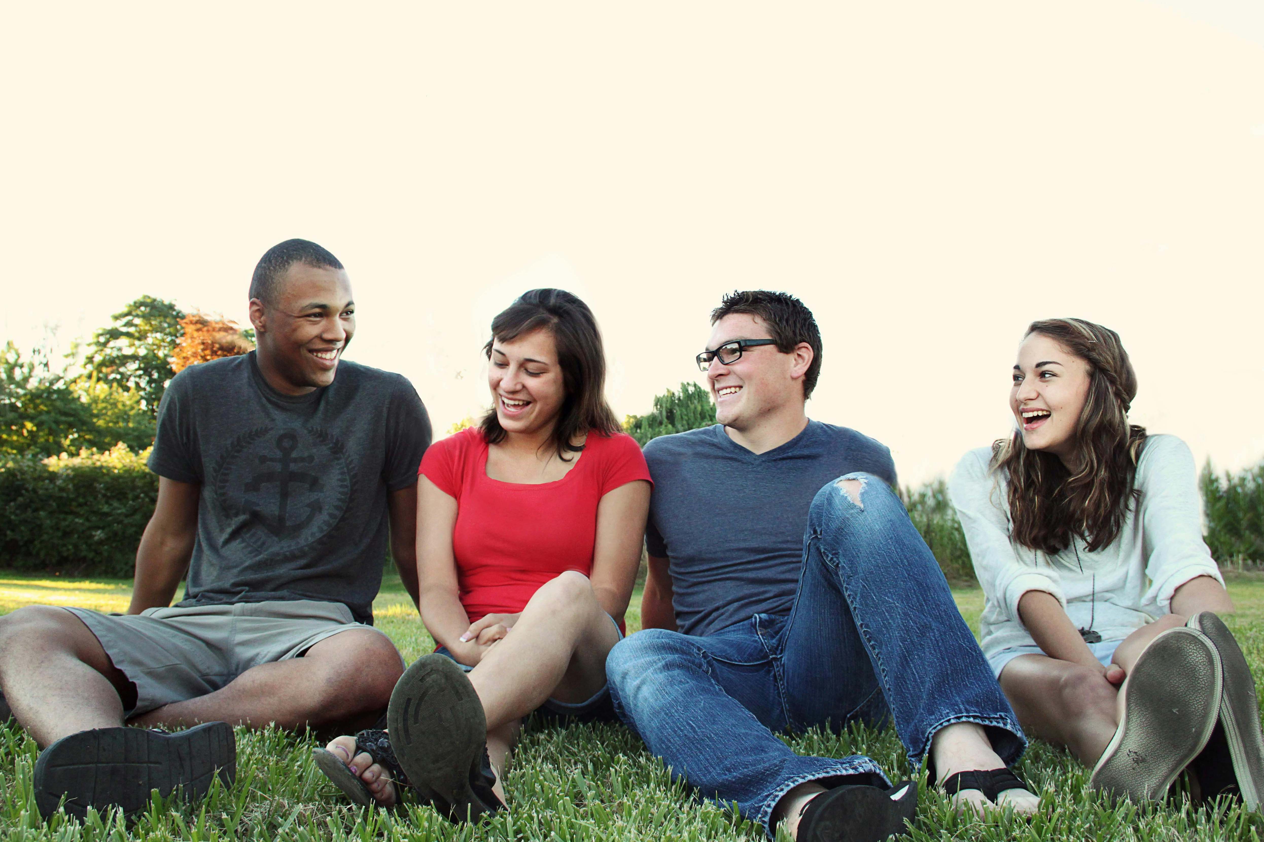 group of diverse friends smiling and sitting next to eachother on grass field