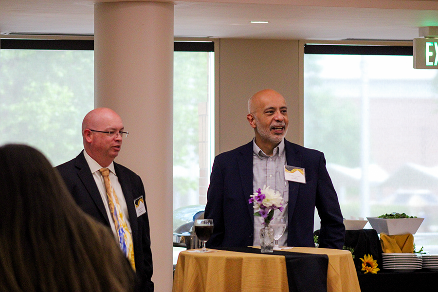 HILP Dinner 2025-2026 / Two men in suits stand by a table with a yellow cloth and floral centerpiece, engaging in conversation at a formal event. The mood is professional and relaxed.