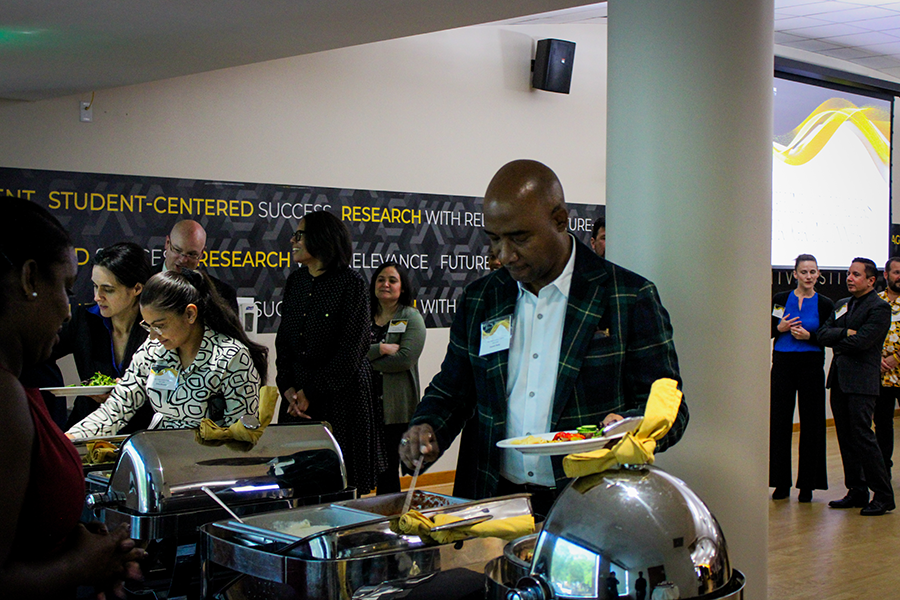 HILP Dinner 2025-2026 / People at a formal event buffet, serving food from chafing dishes. A wall displays key terms like "Student-Centered" and "Research." The atmosphere is social and professional.