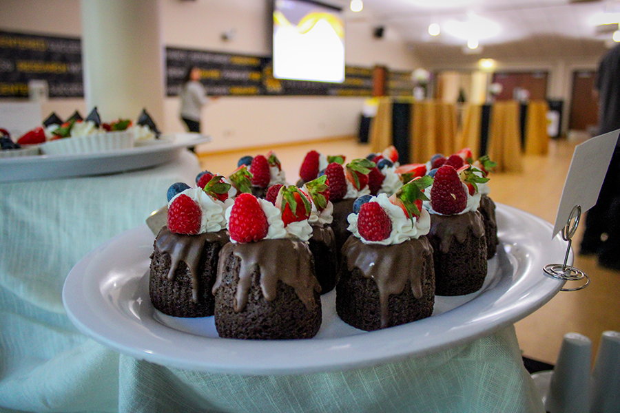 HILP Dinner 2025-2026 / Mini chocolate bundt cakes with whipped cream, raspberries, blueberries, and strawberries on a white plate. Background shows a conference setup.